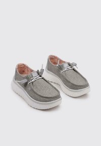 Zapatos casuales gris claro de tejido con un acabado texturizado, suela de goma blanca, cordones elásticos y un interior acolchado.