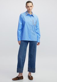 Lichtblauw overhemd met een gestructureerde kraag, versierd met sequins en rhinestones. Gecombineerd met brede denim en schoenen met leopardprint.