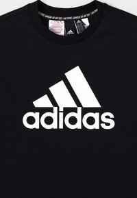 Czarny bawełniany t-shirt z dużym białym logo Adidas z przodu. Materiał jest gładki, a design ma okrągły dekolt.