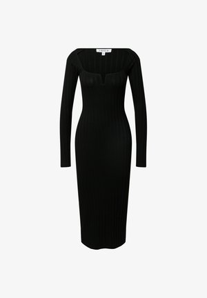 Robe midi noire à côtes avec des manches longues, un décolleté rond et une légère découpe en V. Associée à des mocassins noirs à semelles épaisses et des chaussettes noires.