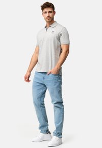 Grå polo skjorte med korte ærmer og en mørk krave, der har et lille logo. Kombineret med lyseblå jeans og hvide sneakers.