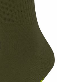 Chaussette vert olive avec une texture côtelée et un talon renforcé. Un logo jaune vif près des orteils ajoute une touche de couleur.