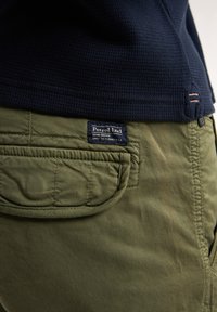 Navy textured top with long sleeves paired with olive green pants featuring a prominent patch pocket and a branded label on waistband.