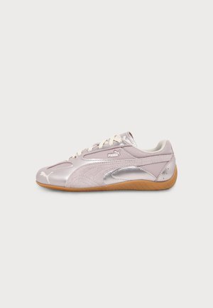 Lyserød Puma-sneaker med hvide snørebånd, metaliske sølv accenter og en brun gummisål, vist i profil på hvid baggrund.