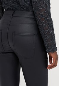 Hoge taille zwarte faux leren broek met een gladde textuur en twee achterzakken, met tonale stiksels op de naden.