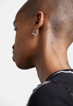 Silver hoop earring adorned with small golden accents, worn in a close-up profile view, showing smooth skin and a tattoo on the neck.