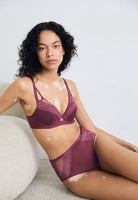 Mauve színű fehérnemű szett, melynek része egy hálós részletekkel ellátott melltartó, állítható pántokkal, valamint magas derekú bugyi texturált részletekkel.