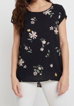 Black short-sleeve top with round neck, featuring scattered pale pink, yellow, and green floral patterns, worn with white pants.
