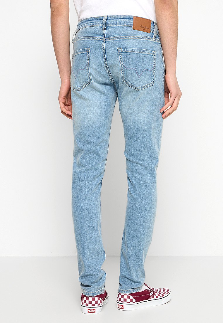 Jeans de mezclilla azul claro con corte recto, que cuentan con un parche de cuero marrón y dos bolsillos traseros con un diseño de puntada en zigzag.