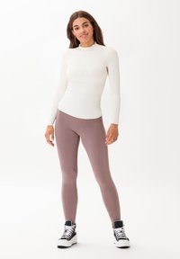 Maglietta bianca a maniche lunghe con scollo scallop, abbinata a leggings morbidi color malva e sneakers alte nere. Design minimalista.