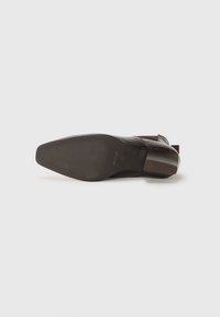 Chaussure en cuir marron avec un bout pointu et un petit talon. Présente une surface texturée et une semelle lisse avec un branding subtil.