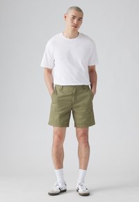 Shorts kaki dintr-un amestec de bumbac, având o croială clasică cu buzunare laterale. Asortați cu un tricou simplu alb din bumbac și șosete atletice albe.
