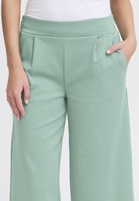 Lichtgroene wijde broek gemaakt van een textuurstof, met een hoge tailleband met plooien en zijzakken. Gladde afwerking.