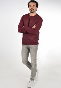Burgunderfarbener Pullover mit strukturiertem Paneeldesign, kombiniert mit hellgrauen, eng geschnittenen Jeans und weißen Sneakers. Einfaches, lässiges Outfit.