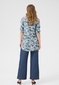 Blomsterbluse i nuancer af blå med trekvartærmer, parret med vide mørk denim jeans. Glat tekstur og bueformet søm.