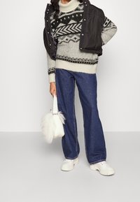 Stickad tröja med geometriska mönster i svart och krämfärgad, matchad med mörkblå vida byxor och en vit väska i konstpäls. Svart väst.