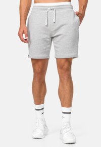 Shorts en coton gris avec une taille élastique à cordon, poches latérales et ourlets cousus. Portés avec des baskets blanches et des chaussettes rayées.