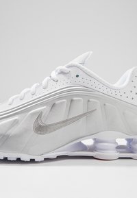 Chaussure de sport blanche avec logo Nike Swoosh gris, tige perforée, semelle amortissante et coussinets visibles absorbant les chocs au talon et à la semelle intermédiaire.