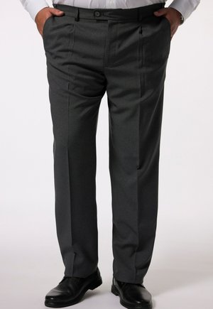 Grijze broek met een rechte band, plooien en twee zijzakken. Stof heeft een subtiele textuur; gecombineerd met zwarte schoenen.
