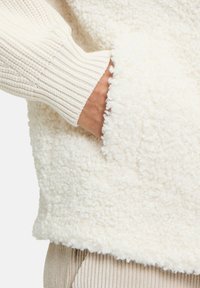 Cremehvid fleecepullover med tekstureret, fluffy overflade, ribbede ærmeafslutninger i cremefarve og en stor frontlomme. Blødt og hyggeligt stof.