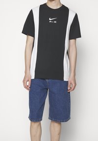 Schwarzes und weißes Nike T-Shirt, kurze Ärmel, kontrastierende Seitenpaneele, mit „AIR“-Logo in Weiß. Kombiniert mit blauen Jeansshorts.