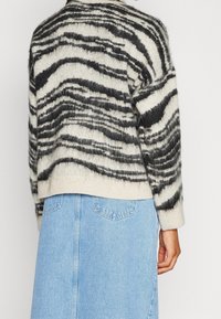Pull en tricot crème avec des rayures en zigzag noires, doté d'une coupe décontractée, de manches longues et d'un ourlet côtelé, associé à une jupe en denim bleu clair.