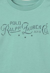 Tyrkysové bavlněné tričko s černým stylizovaným logem "Polo Ralph Lauren & Co." a dekorativními akcenty, s pěti malými hvězdičkami níže.