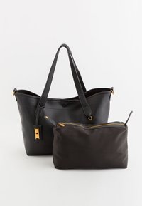 Sort læder tote bag med tekstureret overflade og to hanke, ledsaget af en mindre sort pung med guldlynlås.