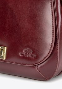 Bordowa skórzana torba o gładkim wykończeniu, z metalowymi akcentami w kolorze złota, wytłoczonym logo oraz usztywnionym kształcie. Posiada staranne przeszycia wzdłuż krawędzi.