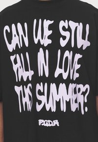 Svart bomulls t-shirt med stor, smältande vit text som lyder "KAN VI FORTFARANDE FÅ FALLA I KÄRLEK DETTA SOMMAR?" och "PGDR" längst ner.