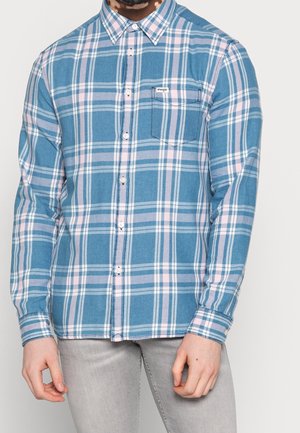Chemise à carreaux bleue avec des lignes roses et blanches, manches longues, poche poitrine et col pointu. Le tissu semble texturé.