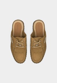 Mocassins slip-on en daim beige avec lacets en cuir, détail de franges sur le dessus et coutures visibles le long des bords, vus de dessus.