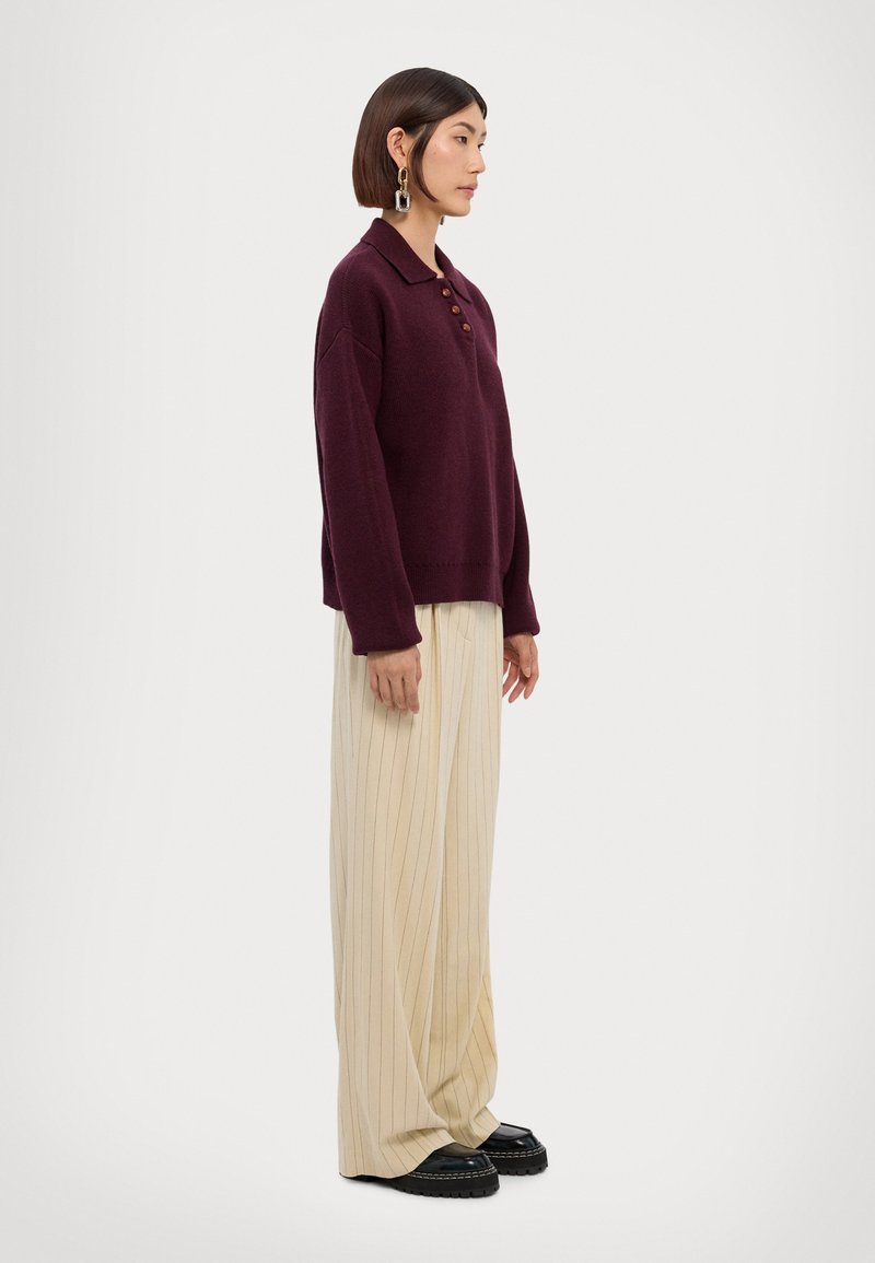 Suéter de punto burdeos con cuello y tres botones, combinado con pantalones de pierna ancha crema a rayas verticales y zapatos de plataforma negros.