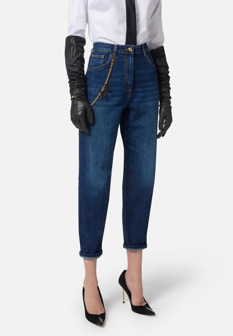 Jeans in denim scuri a vita alta e gamba dritta. Presentano un dettaglio in catena dorata in vita. Abbinati a guanti neri e tacchi.