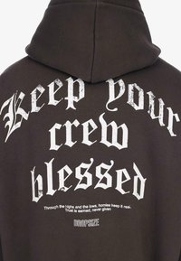 Schwarzer Hoodie mit weißem gotischem Text auf der Rückseite: "Halte deine Crew gesegnet." Kleinere Schrift lautet: "Durch die Höhen und Tiefen, Kumpels bleiben echt."