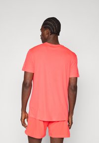 Coral athletic short-sleeve shirt with a crew neckline, lightweight fabric, smooth texture, and an embroidered logo on the left sleeve.