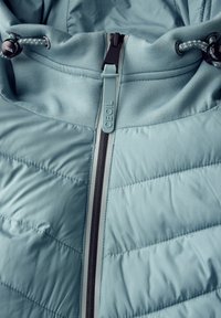 Giacca isolante di colore blu chiaro con zip frontale, caratterizzata da un design a pannelli testurizzati, cappuccio regolabile e dettagli in zip nera a contrasto.