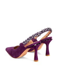 Zapatos de tacón alto de ante morado con punta afilada y parte trasera abierta. Una correa decorativa con acentos brillantes recorre el talón.
