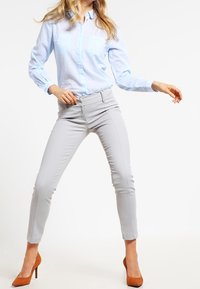 Ljusblå skjorta med knappar och två bröstfickor, i kombination med grå slim fit-byxor och bruna högklackade skor. Rent snitt och skräddarsydd passform.