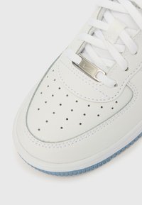 Valge nahast vabaajajalats perforatsiooniga varbalaastal, hõbedased detailid, valged paelad ja hele sinine kummipõhi. Eriline keskosa õmblusdetail.