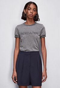 T-shirt grigia aderente con maniche corte e bordi più scuri, che presenta il testo "PATRIZIA PEPE" in un font bold. Abbinato a pantaloni corti a pieghe blu navy.