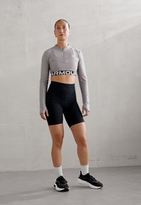 Grå langermet crop topp med glidelås, svarte høyhårede shorts, svarte sneakers og hvite sokker, står på et lys grått gulv.