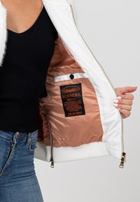 Weißer Bomberjacke mit satin Kupfer-Innenseite, goldenen Reißverschluss und schwarzem Etikett. Rippbündchen und eine weiche Textur innen.