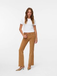 Biała krótka koszulka, brązowe spodnie z korduroy w stylu dzwonów, teksturowany materiał, wysokie buty na obcasie w wężowy wzór, stojąca na jednolitym tle.