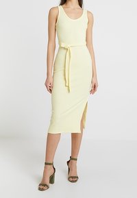 Gul ribbad midi-klänning med tanktoppis stil, bältad midja, sidofåra, ihop med gröna högklackade sandaler.
