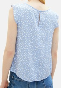 Jasnoniebieska bluzka w drobne białe kwiatowe wzory, miękki materiał, krótkie rękawy, zaokrąglony tylny dół oraz rozcięcie na plecach zapinane na guzik.