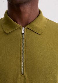 Kurzarm-Poloshirt in Olivgrün, mit einem Reißverschluss vorne, Kragen und gerippter Textur. Sauberes Design ohne sichtbare Muster oder Akzente.