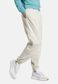 Beige jogger pants with elastic cuffs, side pockets, and a relaxed fit, paired with white sneakers featuring black and gum accents.
