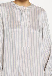 Lehká pruhovaná košile z měkké tkaniny, s vertikálními modro-bílými pruhy, zapínáním na knoflíky u krku a volným střihem pro pohodlí.