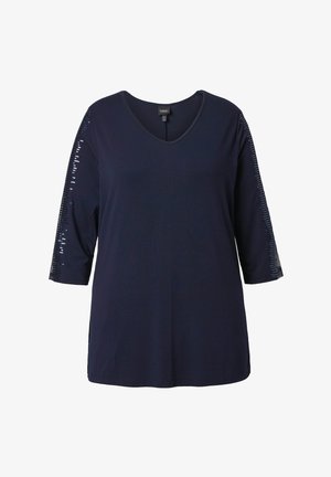 Granatowy top z dekoltem w serek i rękawami do połowy przedramienia, zdobiony linią cekinów biegnącą wzdłuż zewnętrznej strony ramion.